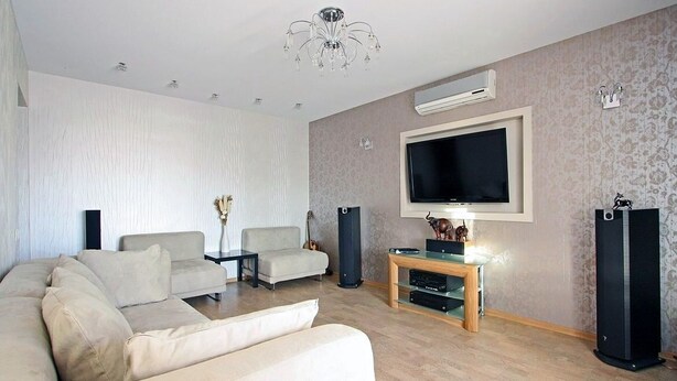 Una sala de estar con un sofá color beige, un televisor, una mesa de centro y un altavoz.