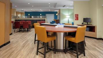A hotel lobby with a round table and chairs, a reception desk, and a seating area with sofas and chairs.