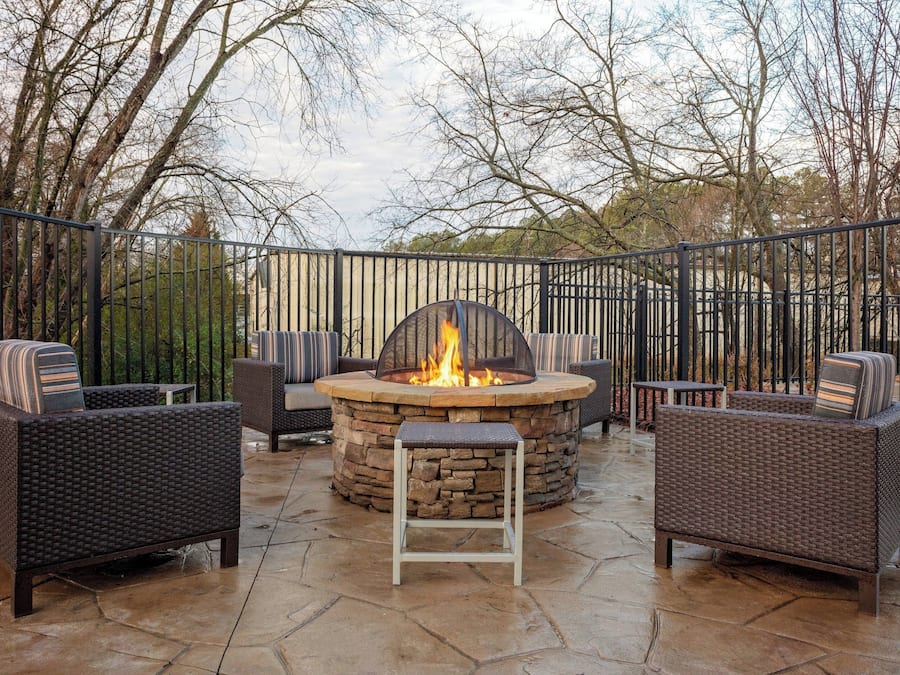 An outdoor patio with a stone fire pit surrounded by wicker furniture and a metal railing.