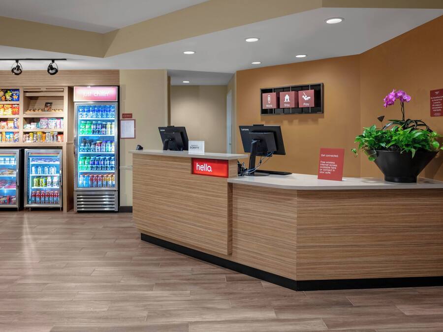 En hotellobby med en receptionsdisk i trä, en skylt med texten ”Ta det lugnt”, en skylt med texten ”hej”, en digital skärm och en växt.