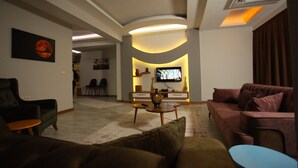 A modern living room with a sofa, armchair, and a TV in the background. - The City Walls Suit Hotel (Diyarbakir)