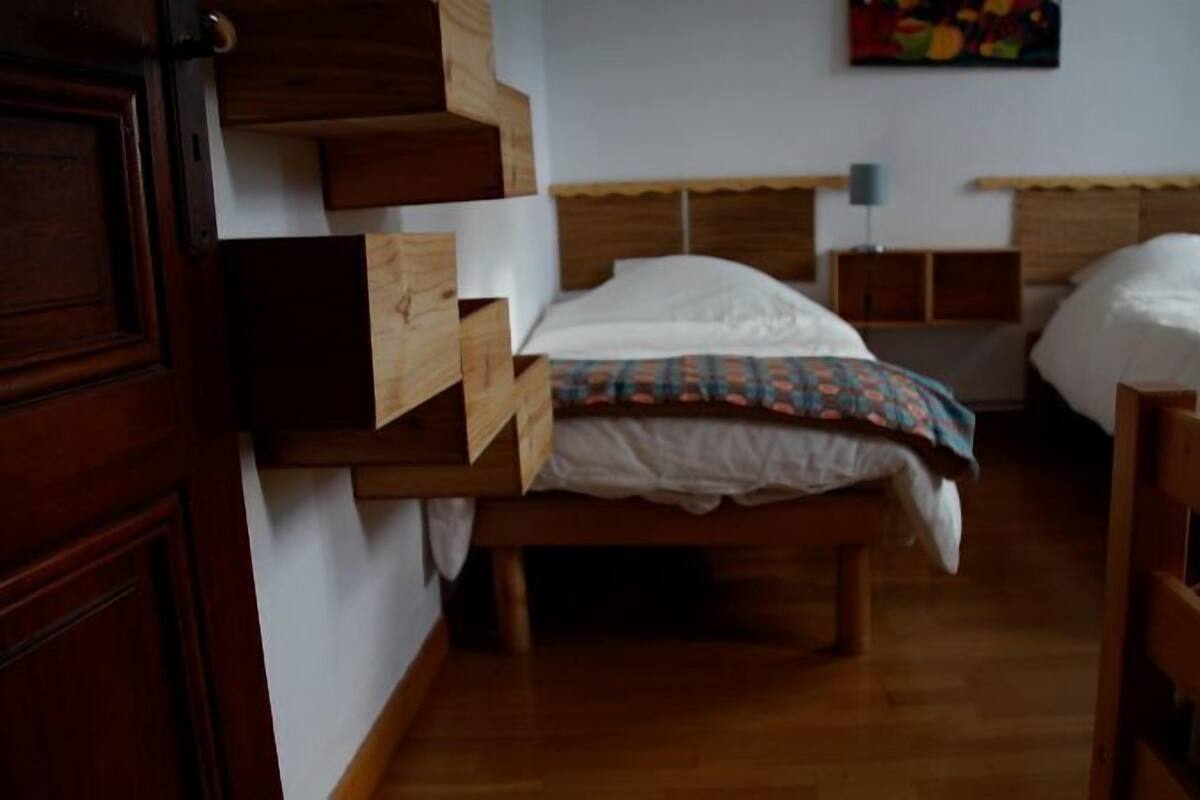 Quarto com duas camas de madeira, um guarda-roupa de madeira e uma pequena mesa.