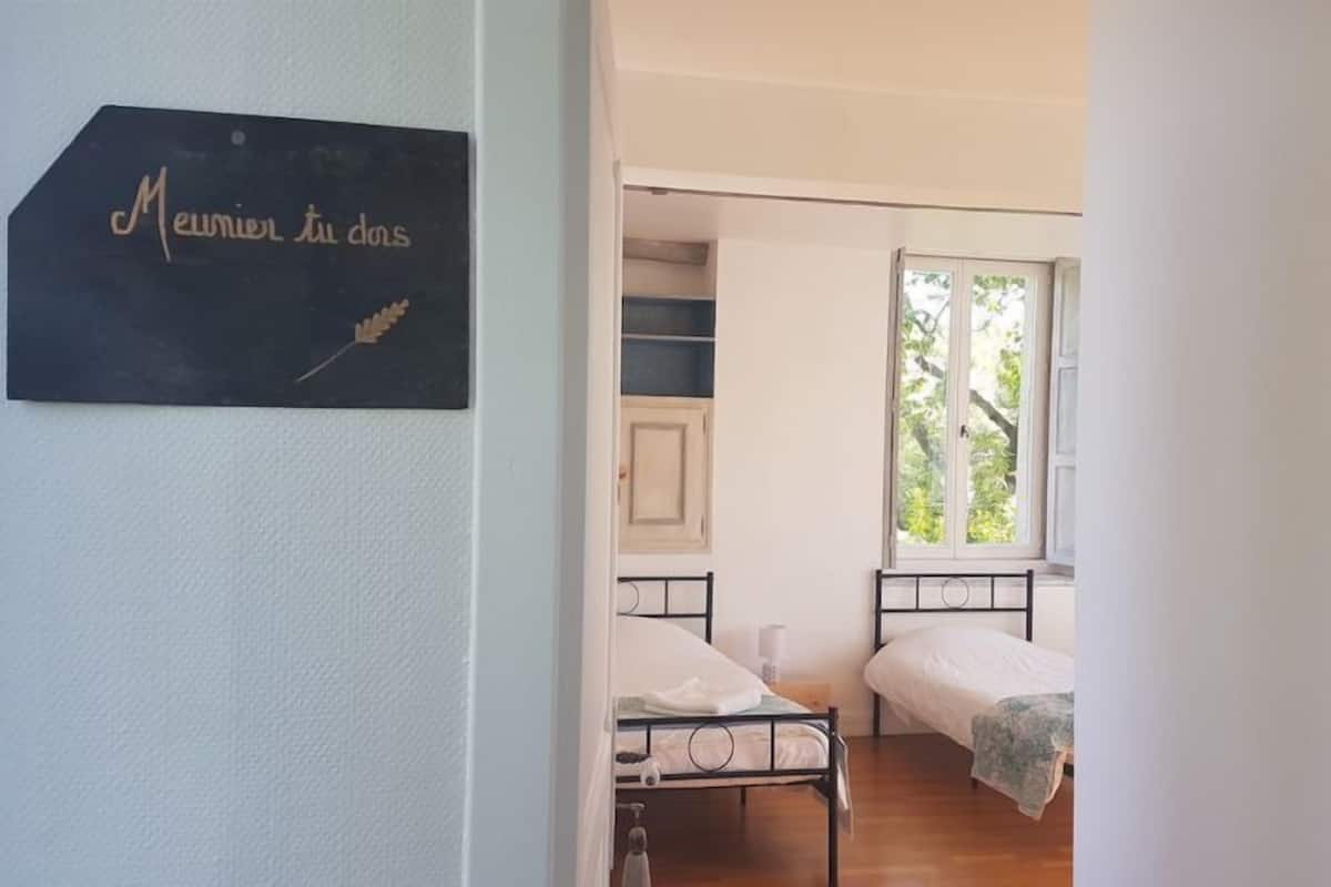 Quarto com duas camas, janela com vista para árvores e placa na parede.