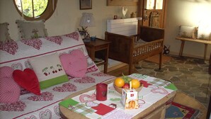Una habitación acogedora con una mesa de madera, un sofá con cojines de diseño de corazón y una pequeña silla de madera.