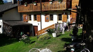 Una mesa redonda con sillas dispuestas al aire libre, rodeada de césped y con una casa al fondo.