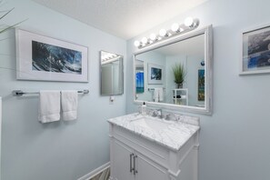 A bathroom with a large mirror, white vanity, and two framed pictures on the wall. - Hip Nautic - Couple's Getaway, Indoor Pool Hot Tub, Walk to Beach, Pickleball (Hilton Head Island)