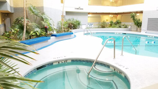 An indoor swimming pool with clear water, surrounded by plants and a white pool deck.