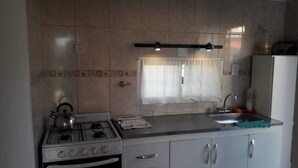 Une cuisine équipée d’une cuisinière à gaz, d’un évier et d’une fenêtre avec des rideaux.
