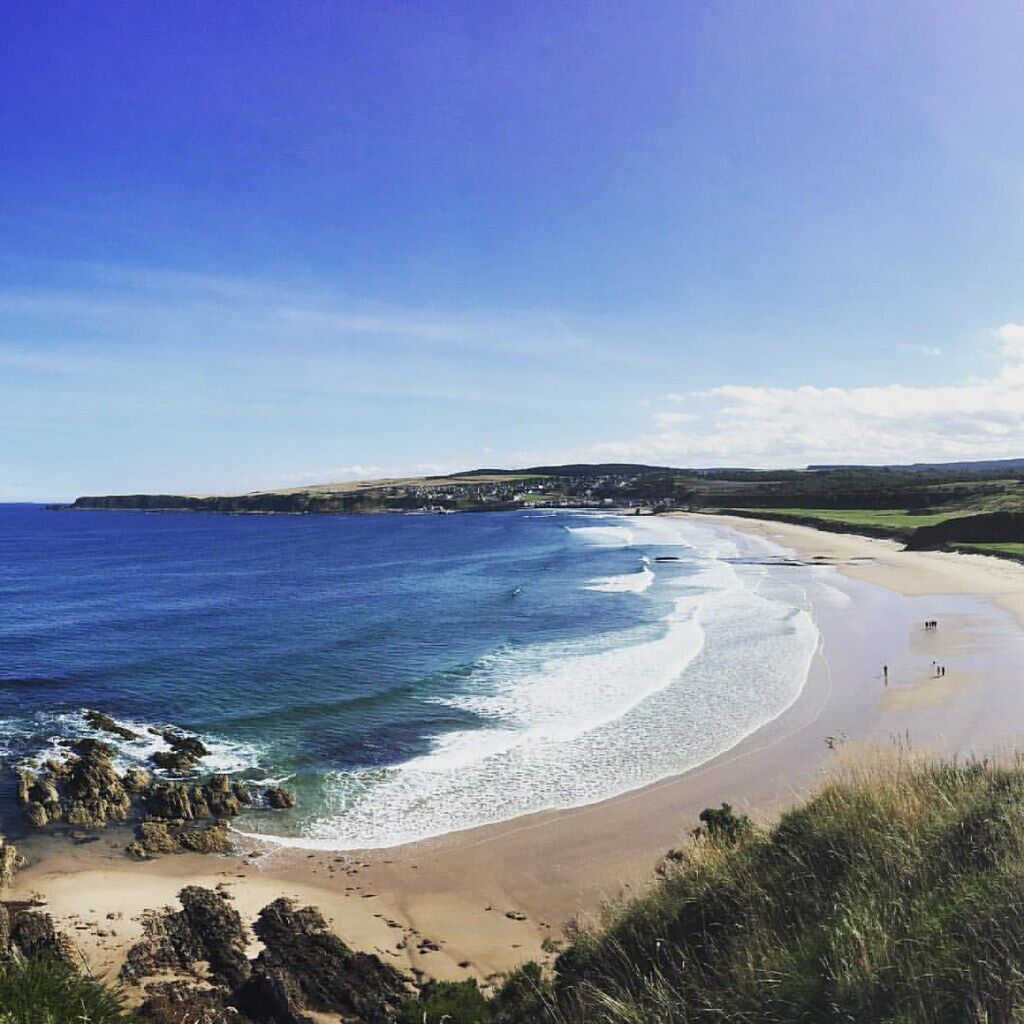 A coastal beach with clear blue waters, sandy shore, and rocky outcrops.