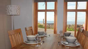 A dining table set for six with grey bowls, wine glasses, and cutlery, overlooking a coastal view. - Modern Fisherman's Cottage with Stunning Uninterrupted Views of the Moray Firth (Findochty)
