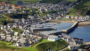 A coastal town with a marina, houses, and a prominent building with a lighthouse. - Modern Fisherman's Cottage with Stunning Uninterrupted Views of the Moray Firth (Findochty)