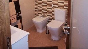 Een badkamer met een betegelde muur in ruitpatroon, een wit toilet, een bidet en een witte wastafel.
