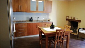 Een kleine keuken met houten kastjes, een eettafel met stoelen, een koffiezetapparaat en een open haard.