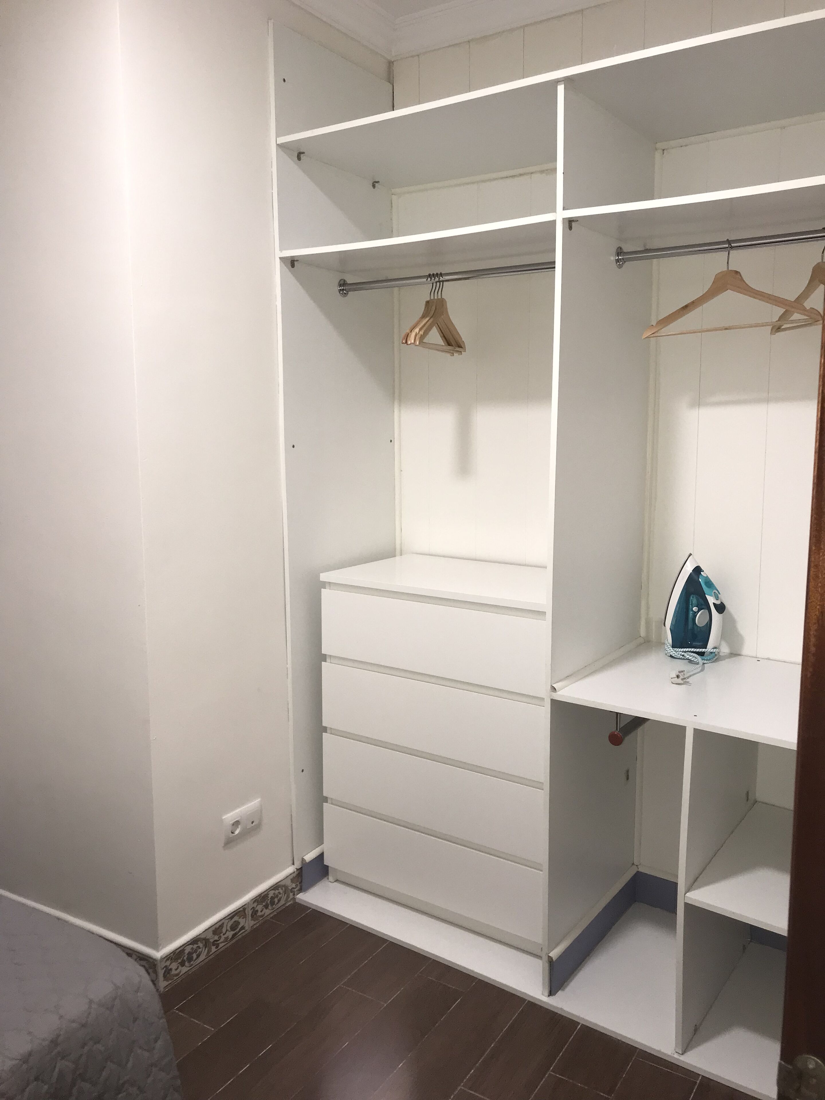 A walk-in closet with open shelving, a hanging rod, and a small ironing station.