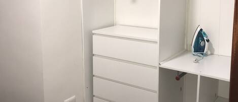 A walk-in closet with open shelving, a hanging rod, and a small ironing station.