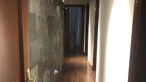 A hallway with a stone wall on one side and a wooden door on the other. The floor is tiled, and the hallway is well-lit with ceiling lights. - Mariñiguez Apartment. (Jerez de la Frontera)