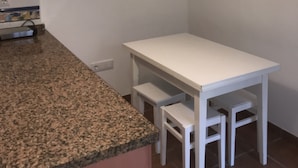 A small kitchen with a granite countertop, white cabinetry, and a white table with two chairs. - Mariñiguez Apartment. (Jerez de la Frontera)