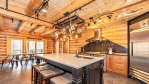 A log cabin interior with a kitchen island, bar stools, wooden cabinets, and a large refrigerator.