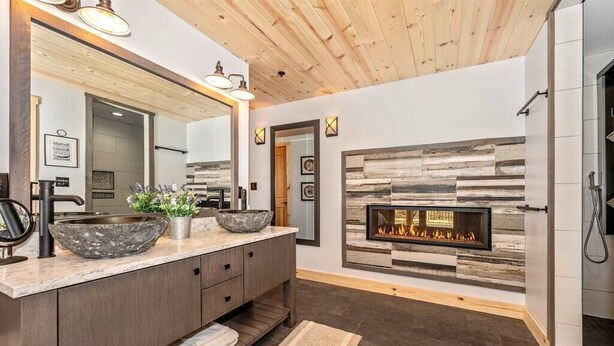 A modern bathroom with a large mirror, two sinks, a fireplace, and a shower area.