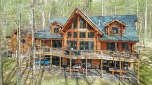 A log cabin with a deck, multiple windows, and a green roof.