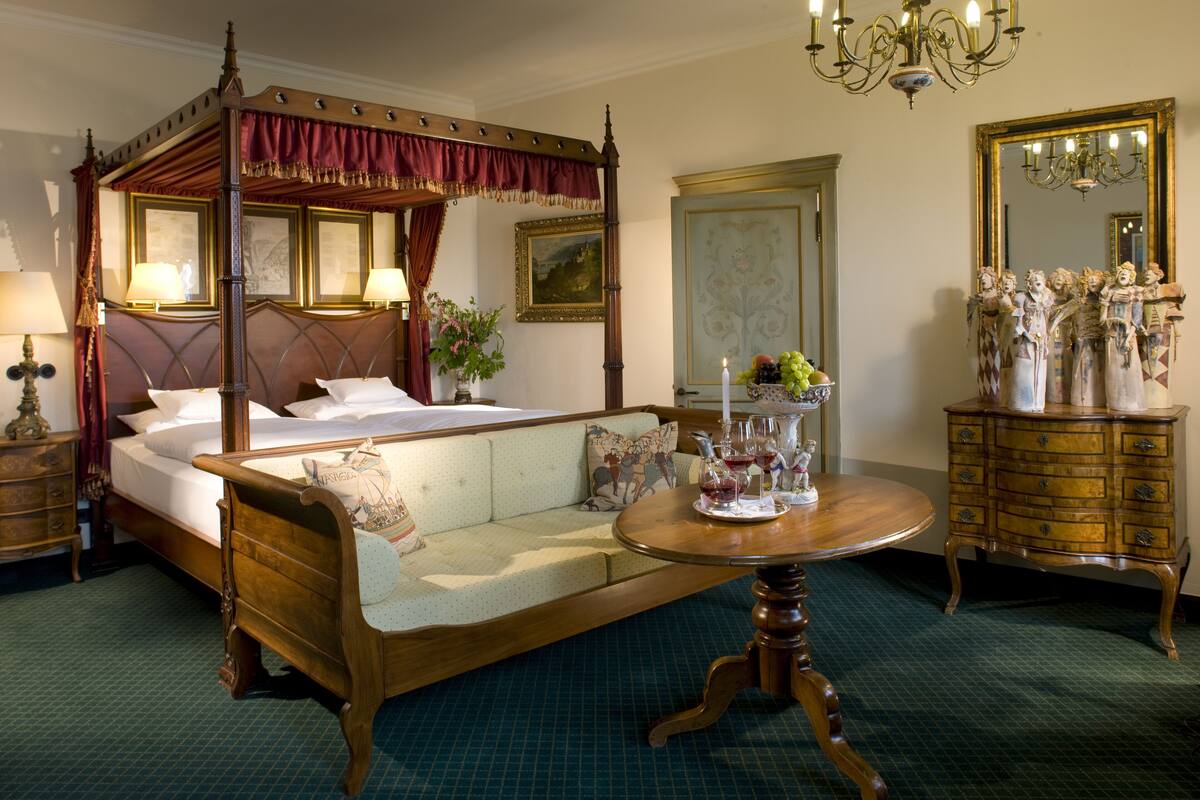 A four-poster bed with a canopy, a round wooden table, a dresser with figurines, and a mirror.