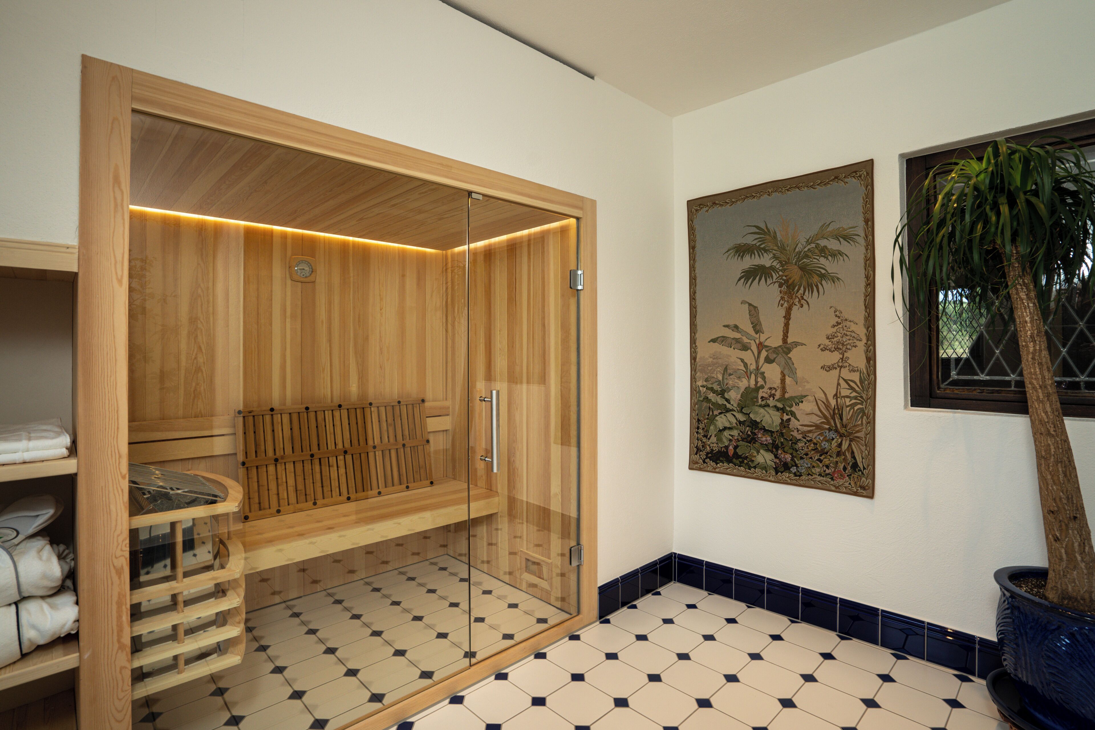 Un sauna en bois doté de portes en verre, d’un sol carrelé et d’un tableau botanique encadré accroché au mur.