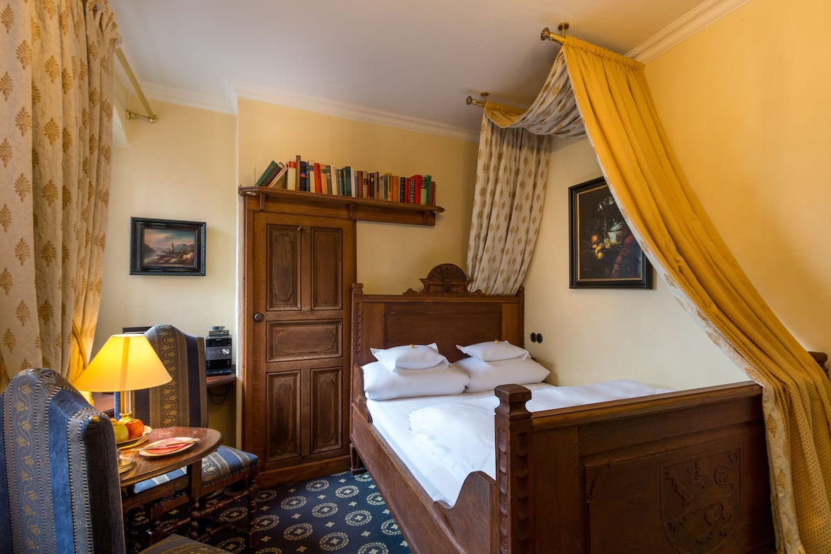 A traditional room with a wooden bed, a small table with a lamp, a chair, and a shelf with books.