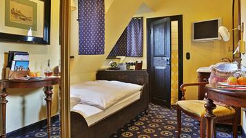 Habitación de hotel con cama, escritorio con ordenador, silla, pequeña mesa con manzanas y un vaso, y baño visible a través de una puerta abierta.