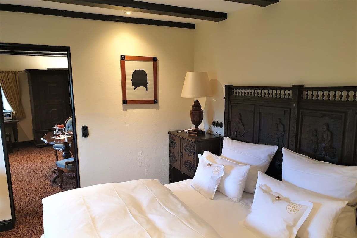A neatly made bed with white linens and pillows, a wooden nightstand with a lamp, and a framed picture on the wall.