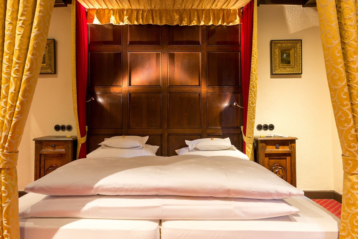 A hotel room with a large bed, wooden headboard, two bedside tables, and a red curtain.