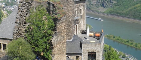 A historic stone building with a turret and a large dome, overlooking a river and hills.