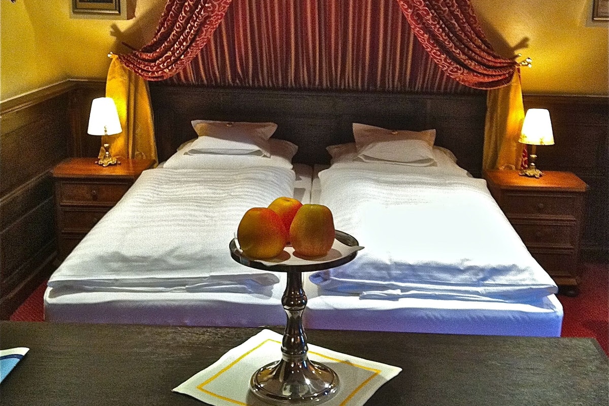 A hotel room with a four-poster bed, a canopy, two bedside lamps, and a fruit bowl on the nightstand.