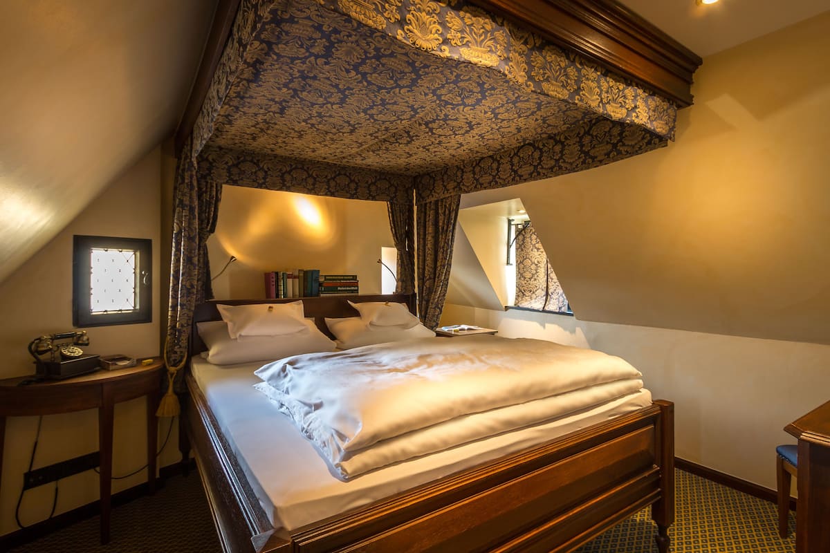 A bedroom with a large bed, a nightstand with a lamp, and a window with curtains.