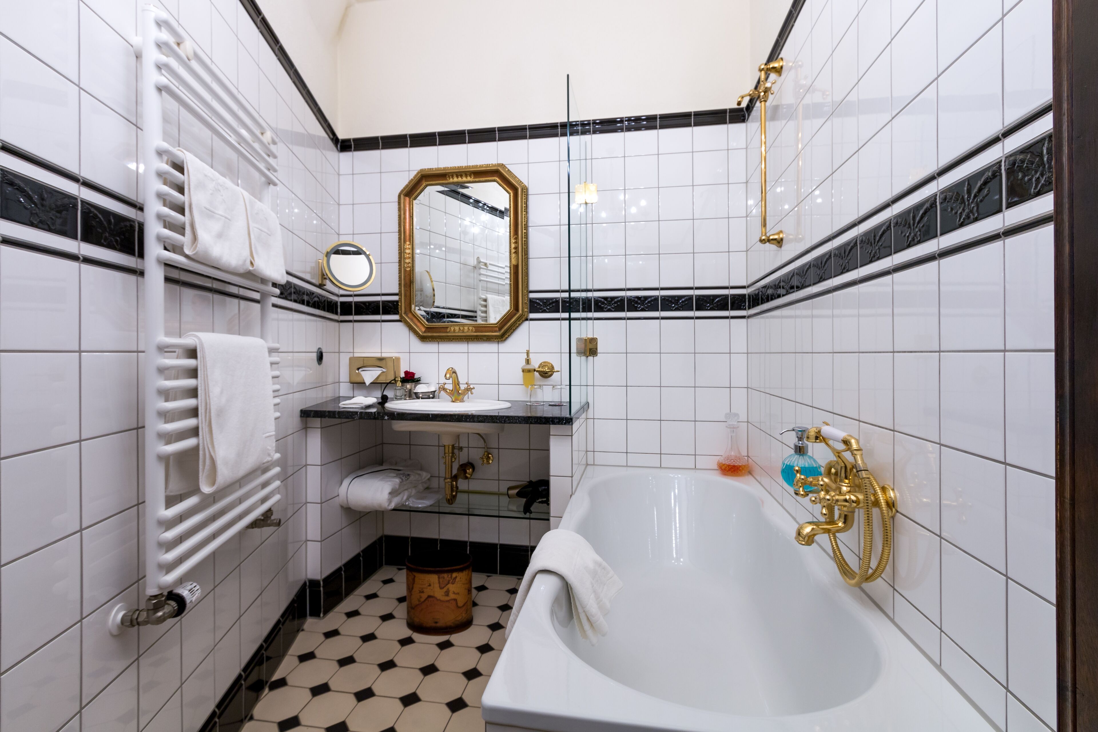 Un baño con una bañera blanca, un lavamanos con detalles dorados, un perchero y un espejo con marco dorado.