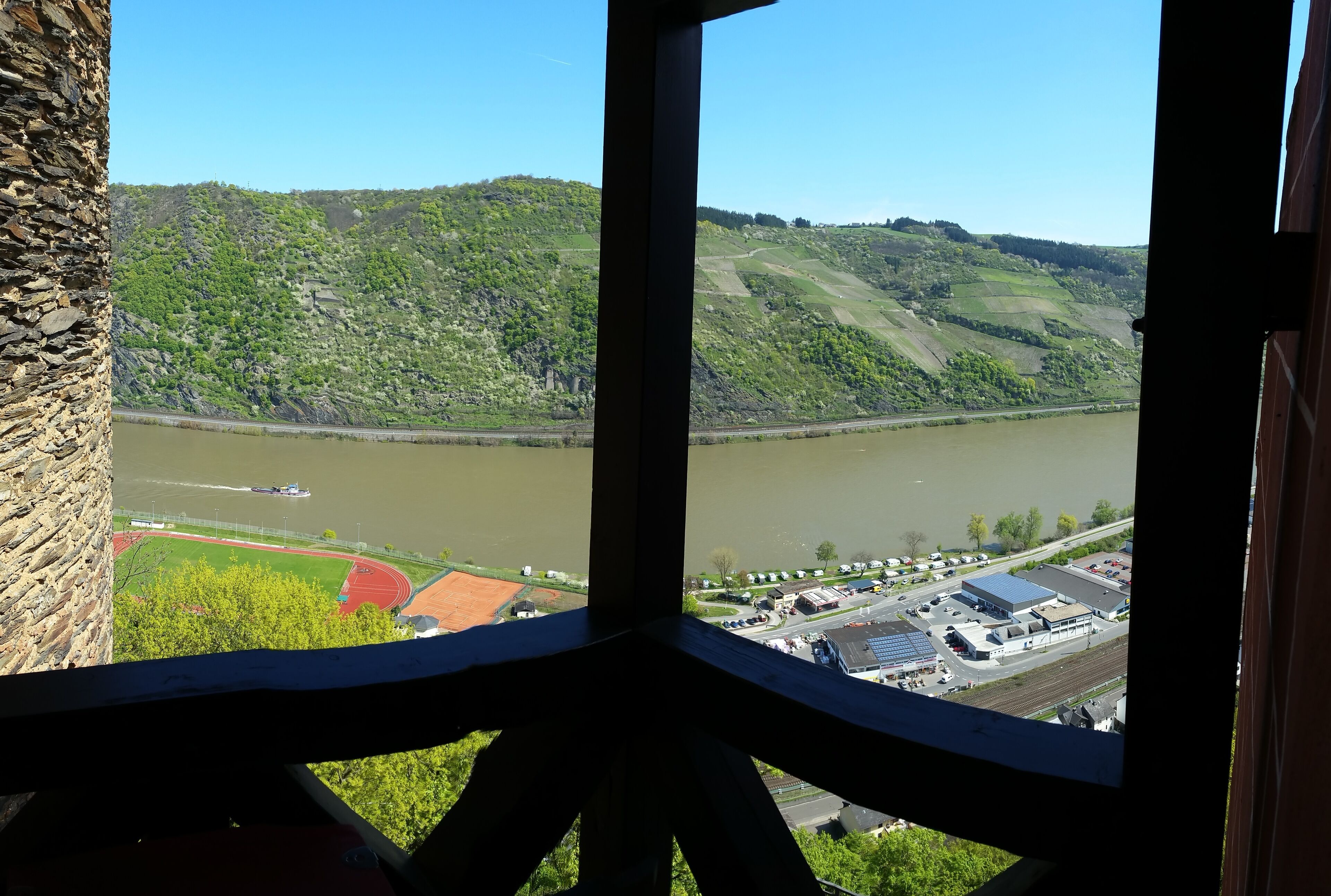 Blick aus einem Fenster auf einen Fluss, grüne Hügel und ein Sportplatz.