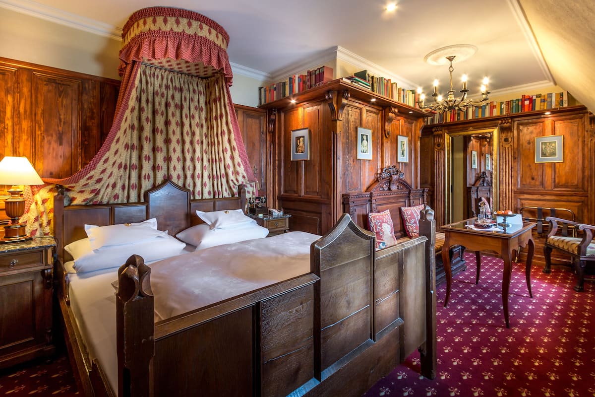 A traditional bedroom with a canopy bed, wooden furniture, and a bookshelf filled with books.