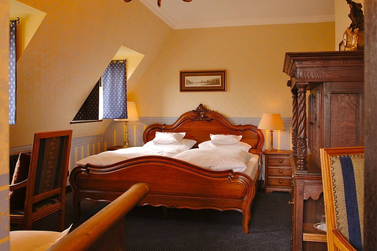 A hotel room with a wooden bed, a chandelier, a framed picture on the wall, and a wooden dresser.