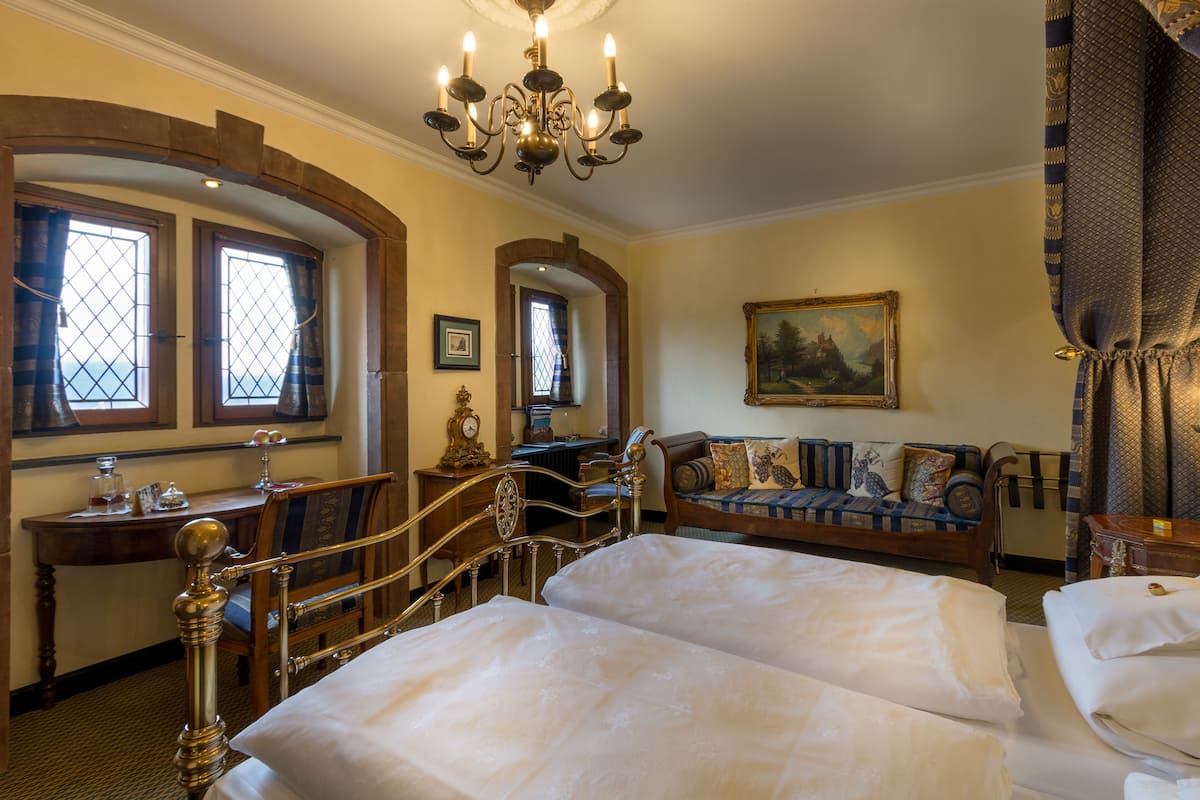 A hotel room with a double bed, a wooden desk, a sofa, and a chandelier.