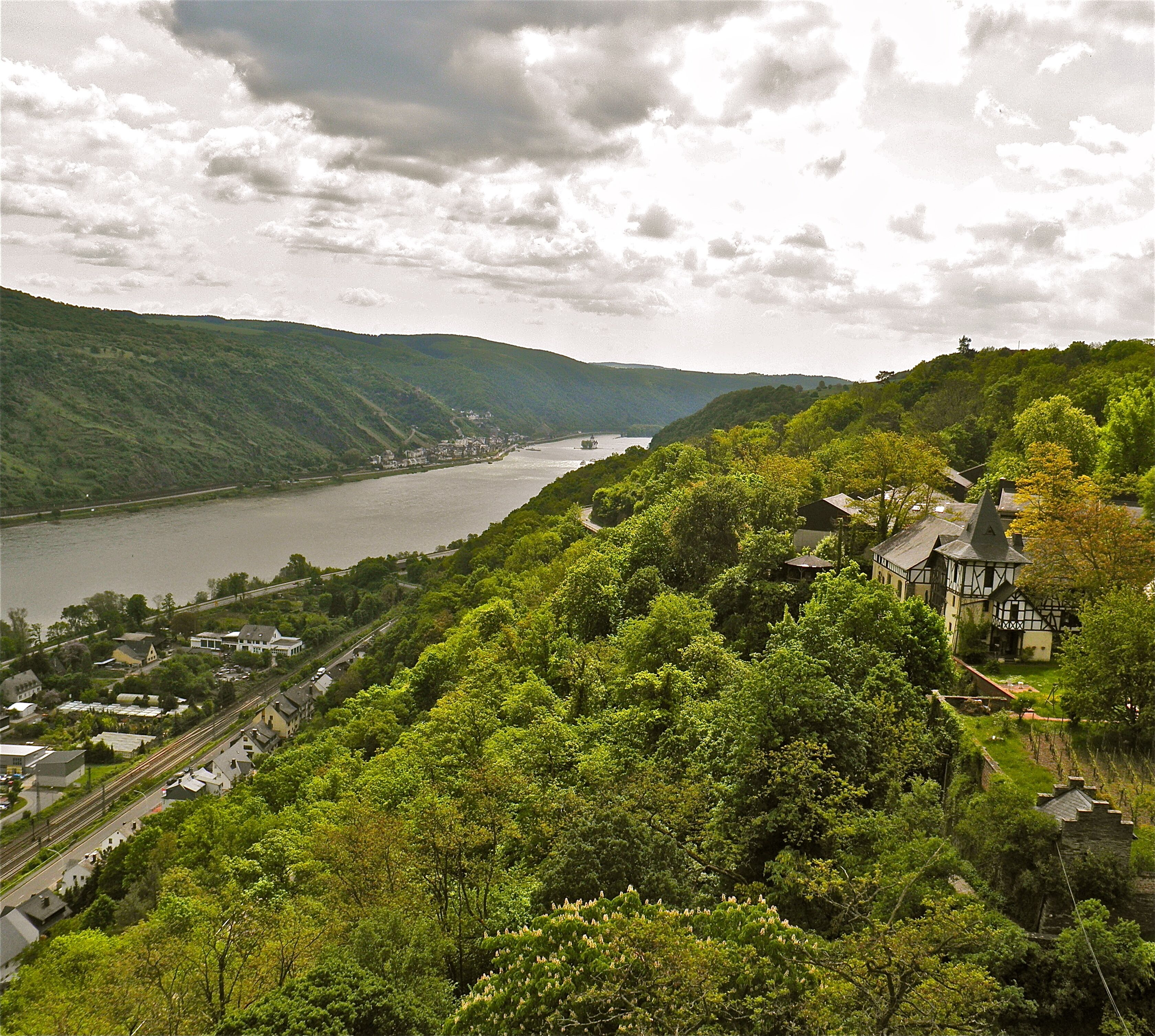 A riverside town with a prominent building featuring a tower, surrounded by lush greenery and a river.