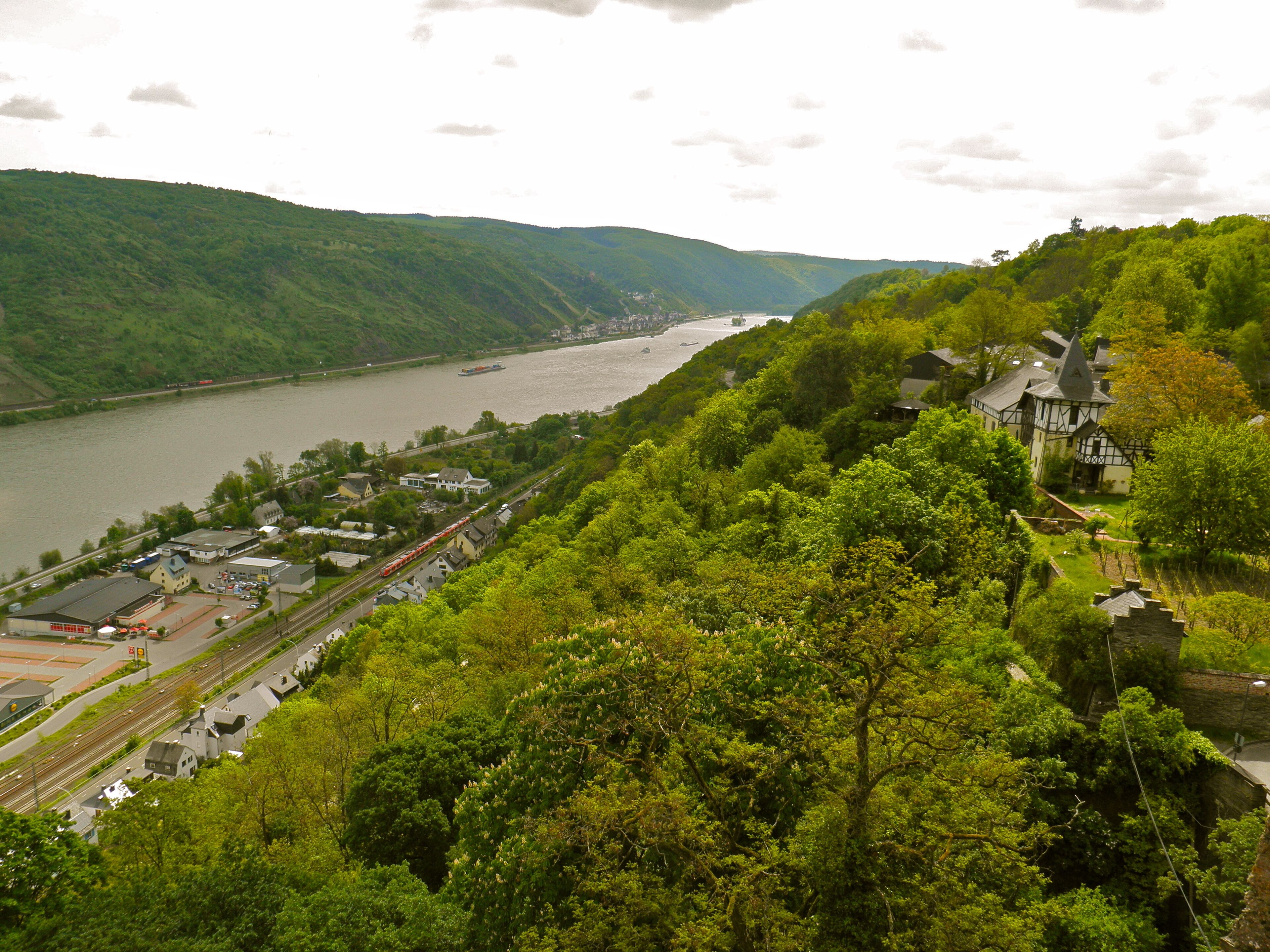A riverside town with a historic building, a train track, and lush greenery.