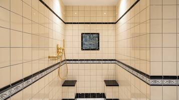 A modern bathroom with tiled walls, a gold shower fixture, and a framed artwork on the wall.