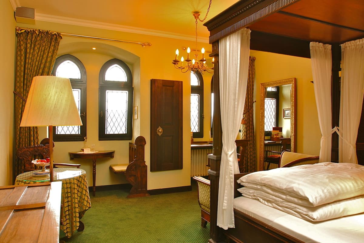 A traditional room with a four-poster bed, a chandelier, and a green carpet.
