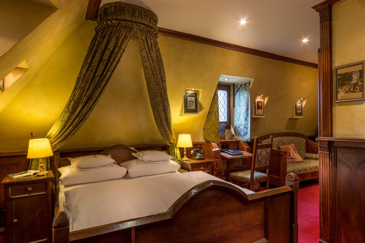 A traditional bedroom with a canopy bed, bedside lamps, a desk, and a chair.