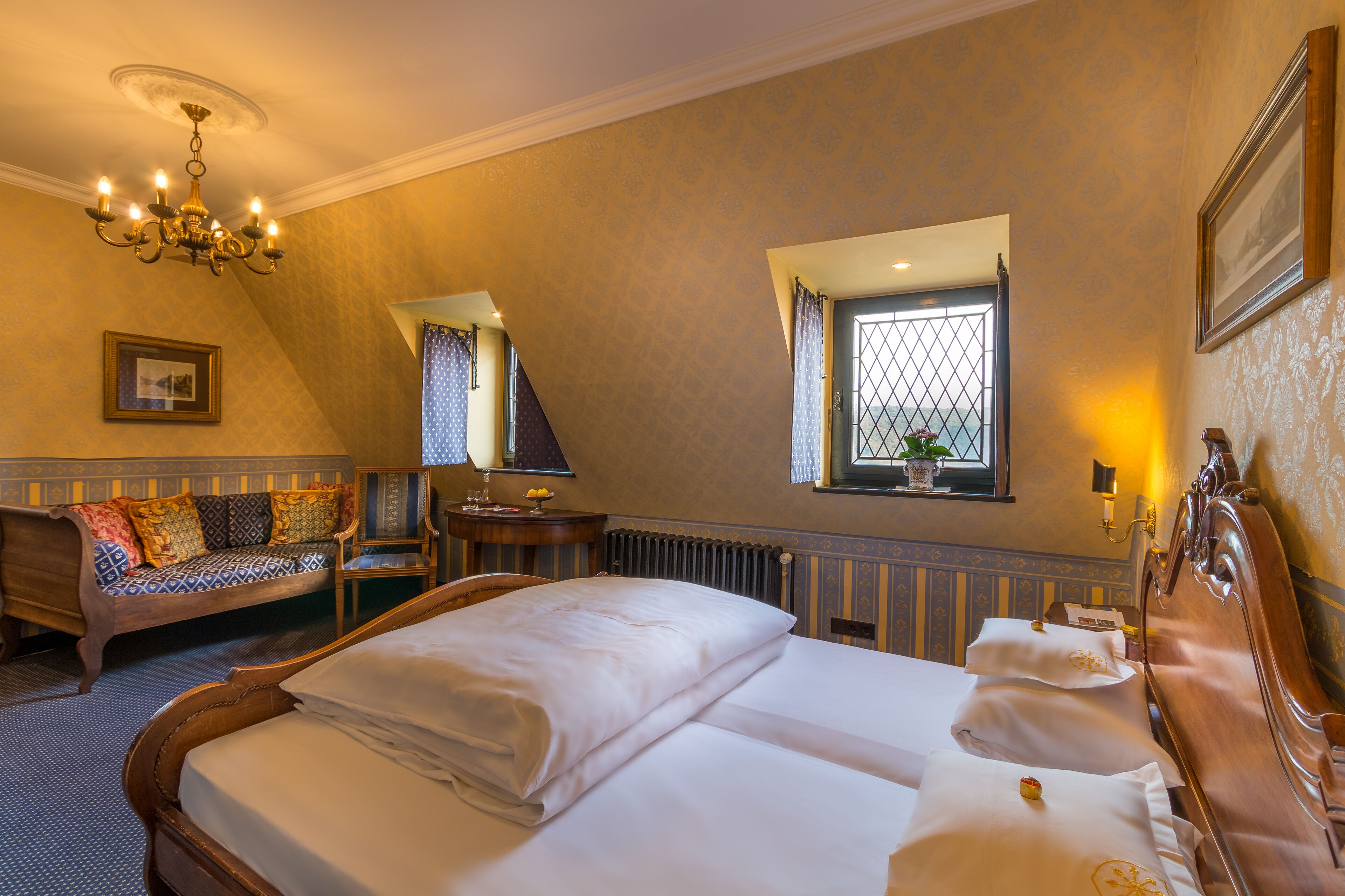 A hotel room with a large bed, a sofa, a small table with a lamp, and a window with curtains.