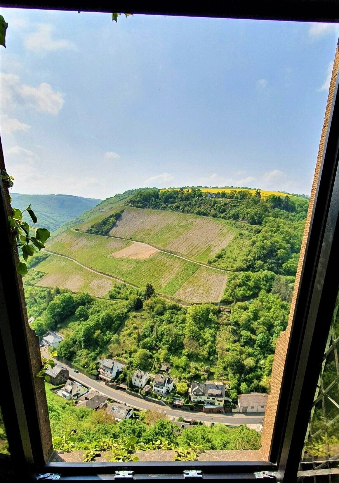 A view from a window overlooking a rural landscape with fields, a road, and houses.