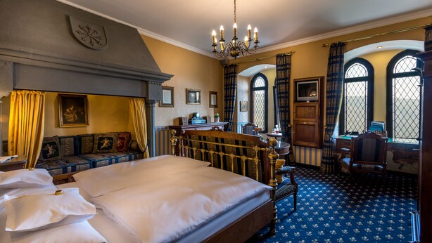 Habitación tradicional con una cama grande, un escritorio y vistas al exterior a través de ventanales abovedados.