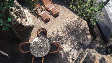 Un patio exterior con una mesa redonda y cuatro sillas, rodeado de pavimento adoquinado y árboles.