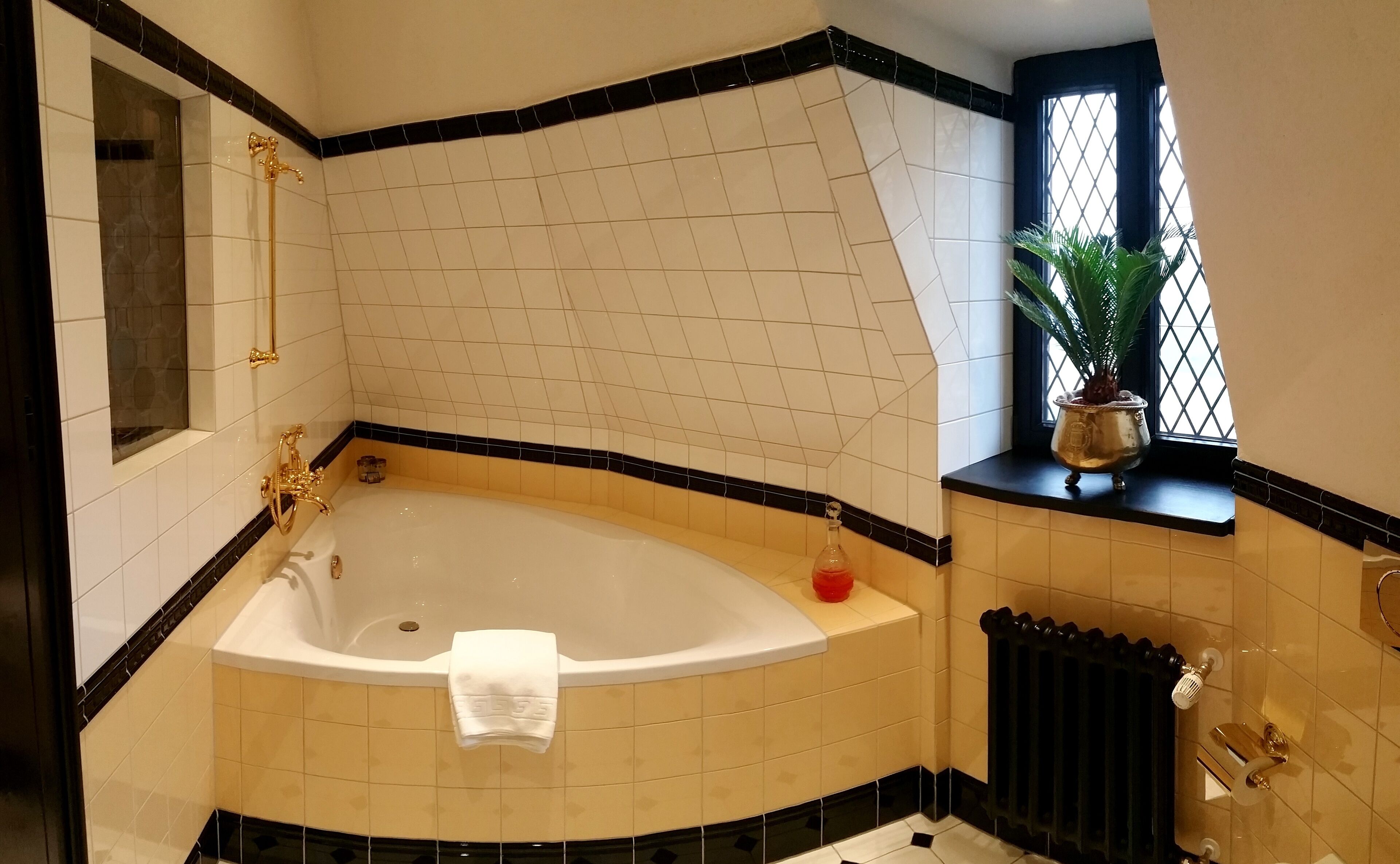 Un baño en esquina con una bañera independiente, una ventana con una planta y un radiador.