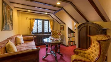 Una habitación tradicional con alfombra roja, sofá de madera, sillón tapizado, una mesa de cristal, una estantería y una puerta de madera grande.