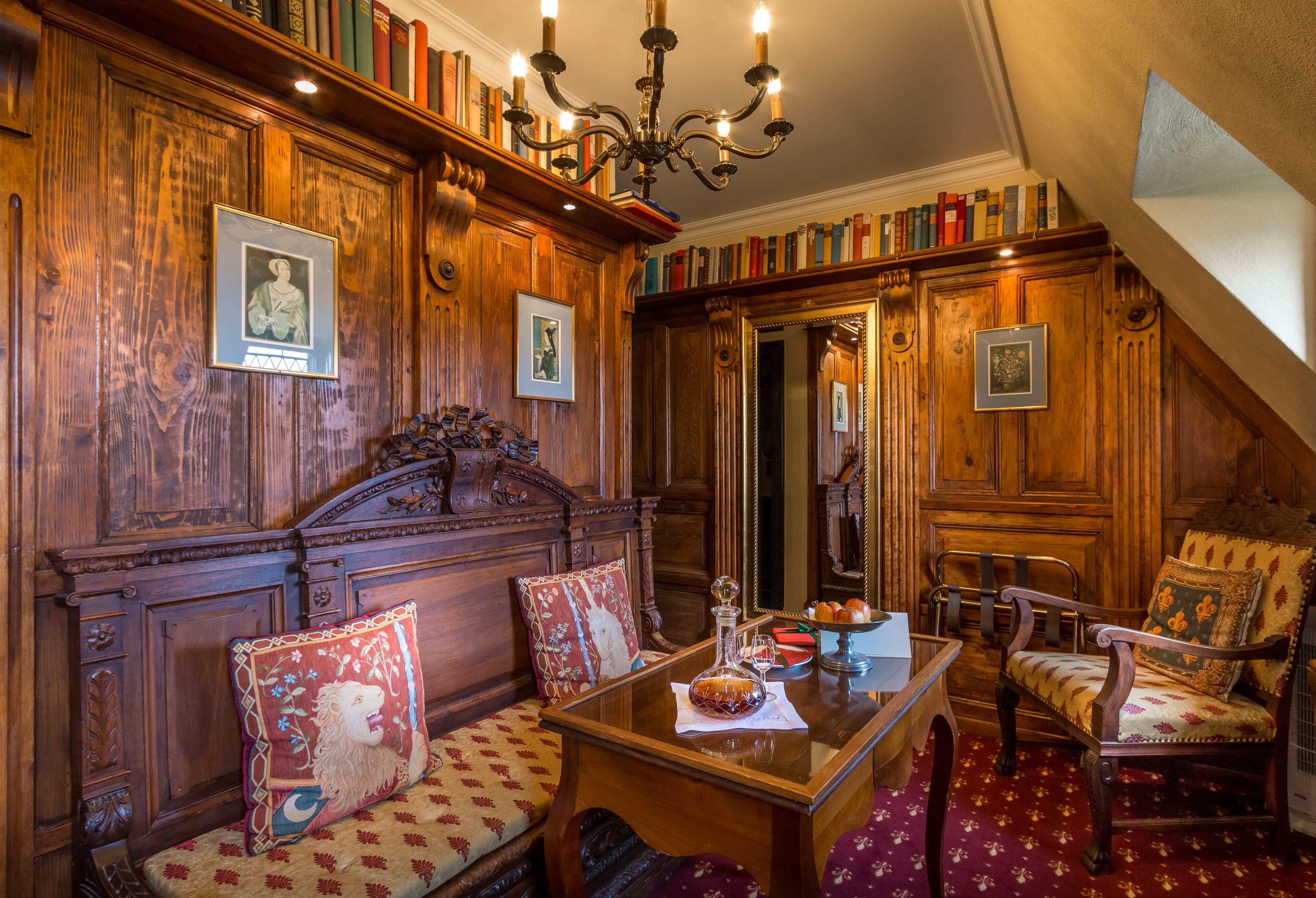 A room with wooden paneling, a chandelier, a wooden table with a decanter, and a bookshelf filled with books.